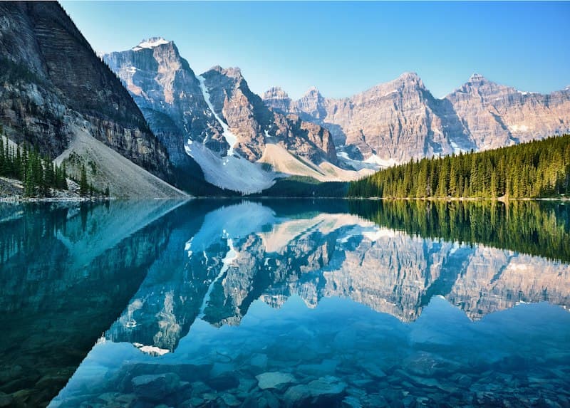 Turquoise glacial waters of Moraine Lake bordered by rugged Rocky Mountain pine peaks in Banff